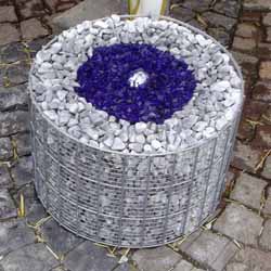 Gabionenbrunnen mit blauem Glassplitt dekoriert